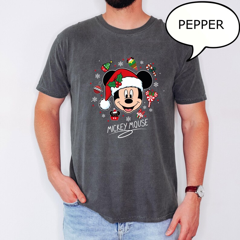 May include: Dark gray t-shirt featuring a festive Mickey Mouse design. Mickey is wearing a Santa hat and surrounded by Christmas ornaments and candy canes. The words "Mickey Mouse" are written below the graphic.