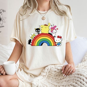 Pode incluir: Uma camiseta branca com um arco-&iacute;ris e personagens de desenhos animados. Os personagens incluem Hello Kitty, My Melody, Keroppi e um cachorro amarelo.