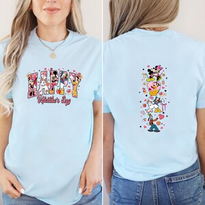 May include: Light blue t-shirt featuring the text "HAPPY Valentine's Day" with Disney characters. The back of the shirt has a vertical design of Disney characters. The shirt is made of a soft material.