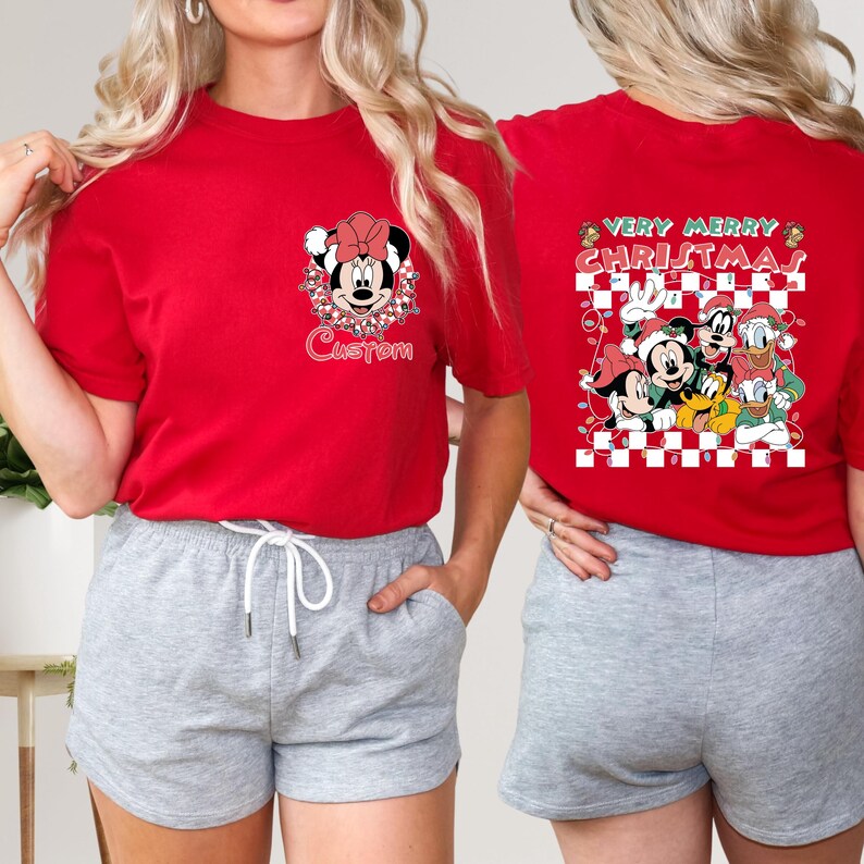 May include: Red t-shirts featuring Christmas-themed Disney characters. One shirt has Minnie Mouse with the word "Custom" below. The other shirt has Mickey, Donald, Goofy, and Pluto with "Very Merry Christmas" text.
