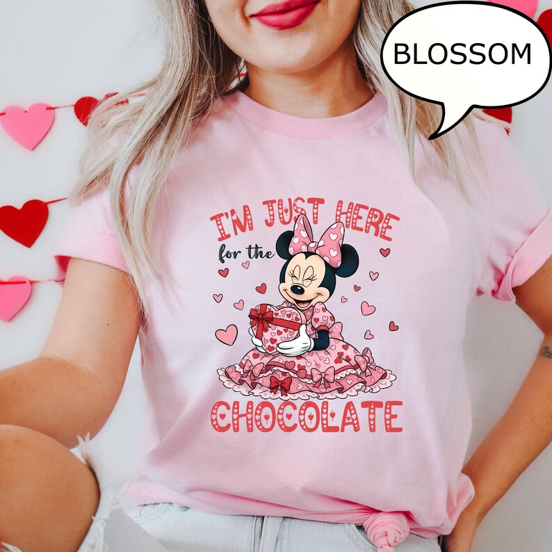 Puede incluir: Camiseta rosa con Minnie Mouse sosteniendo una caja de bombones en forma de coraz&oacute;n. El texto "I'M JUST HERE for the CHOCOLATE" es rojo. Tambi&eacute;n es visible un bocadillo con la palabra "BLOSSOM".