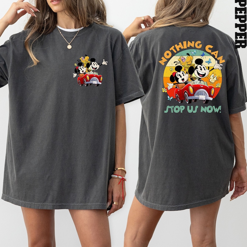 以下が含まれることがあります： グレーのオーバーサイズTシャツ。ヴィンテージなミッキーマウス、ミニーマウス、プルートが赤い車に乗っているカートゥーン画像がプリントされています。Tシャツの背面には「Nothing Can Stop Us Now!」というテキストと、車に乗っているキャラクターの同様のヴィンテージなカートゥーン画像がプリントされています。