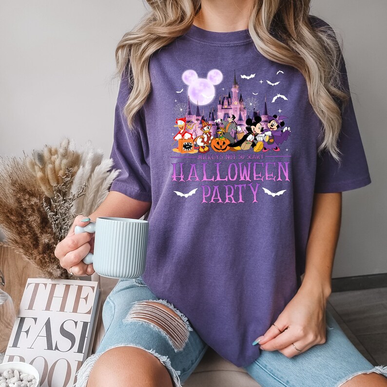 May include: Purple t-shirt with a graphic of Mickey Mouse and friends in front of the Disney castle. The text "Mickey's Not So Scary Halloween Party" is printed on the shirt.