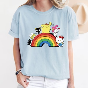Pode incluir: Uma camiseta azul claro com um arco-&iacute;ris e personagens de desenhos animados. Os personagens incluem um cachorro amarelo, um gato preto, um coelho rosa, um sapo verde e um gato branco com um la&ccedil;o vermelho.