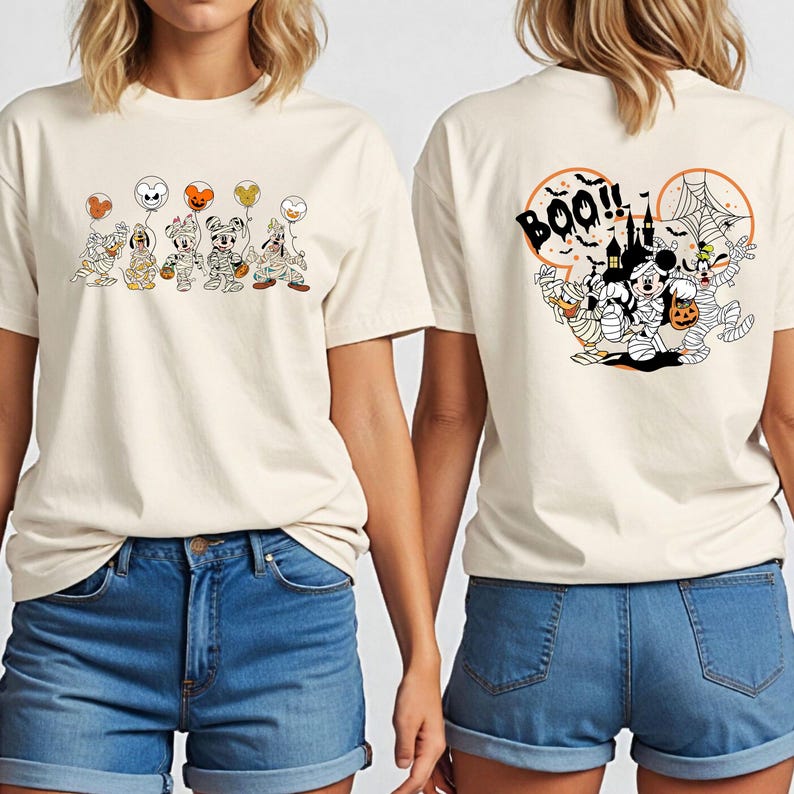 Puede incluir: Camiseta color crema con un dise&ntilde;o de Halloween. La parte delantera muestra personajes de dibujos animados disfrazados de momias sosteniendo globos. La parte trasera de la camiseta tiene un dise&ntilde;o espeluznante con la palabra "Boo!!" y m&aacute;s personajes.
