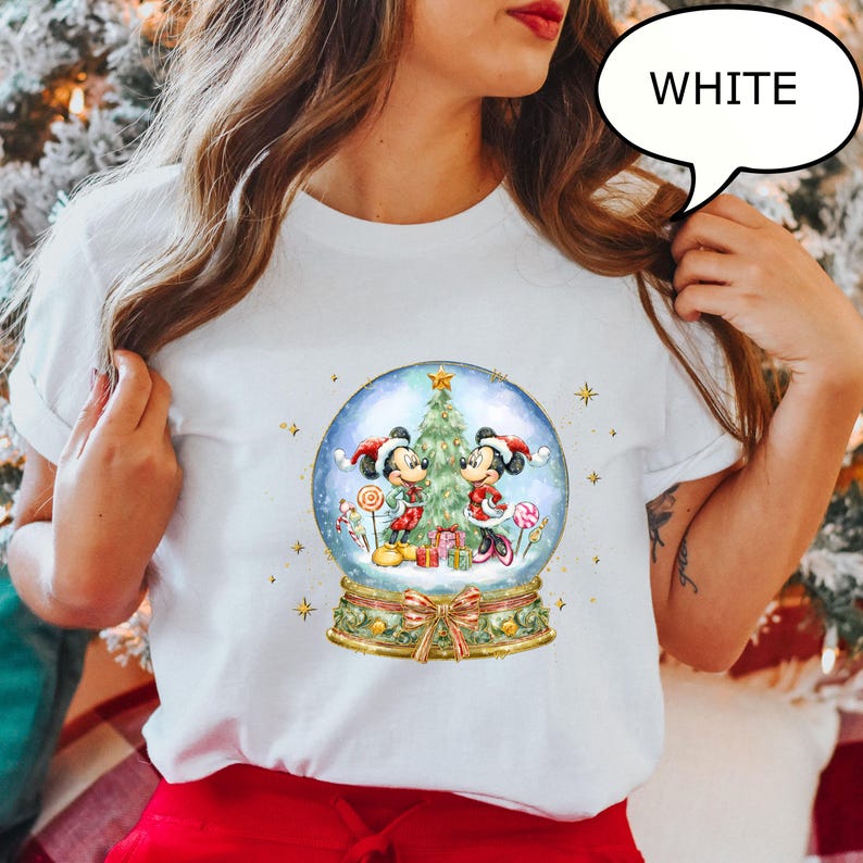 May include: White t-shirt featuring a snow globe design with Mickey and Minnie Mouse in festive attire. The snow globe includes a Christmas tree, gifts, and candy canes. The word "WHITE" is in a speech bubble.
