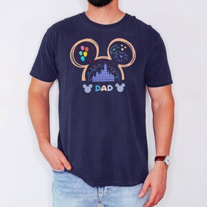 Pode incluir: Uma camiseta azul marinho com um gr&aacute;fico de orelhas do Mickey Mouse com uma silhueta do castelo da Cinderela dentro. O texto "DAD" est&aacute; abaixo do castelo.