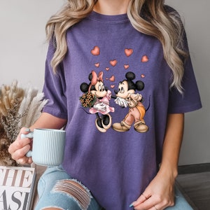 May include: Purple t-shirt with a graphic of Mickey Mouse and Minnie Mouse holding hands with hearts around them.