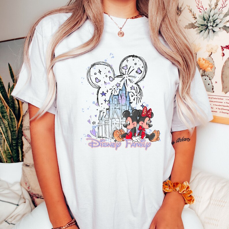 May include: White t-shirt featuring a purple and blue illustration of Mickey and Minnie Mouse in front of Cinderella's Castle with fireworks. The text "Disney Family" is printed below the illustration.