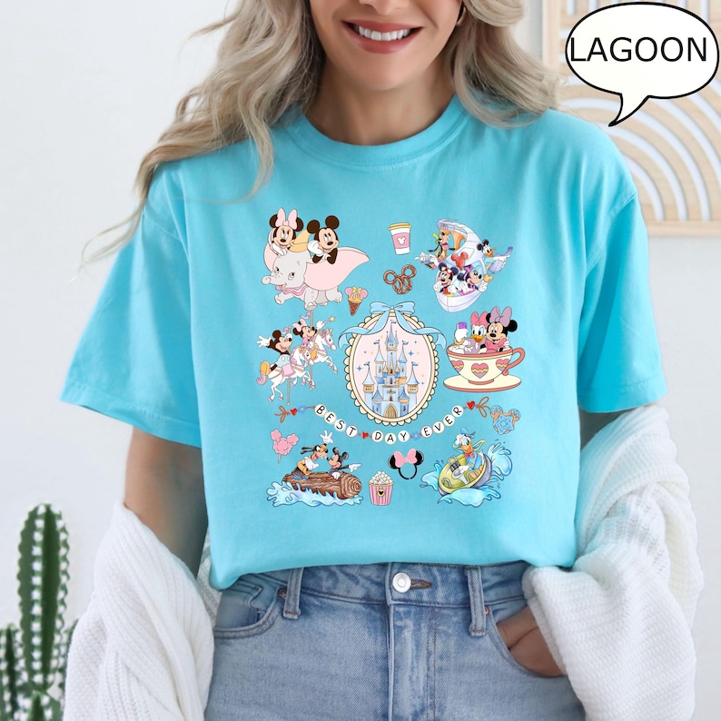 Puede incluir: Camiseta azul claro con varios personajes de dibujos animados y el texto "Best Day Ever". La camiseta tiene cuello redondo y mangas cortas. El gr&aacute;fico incluye im&aacute;genes de un castillo, tazas de t&eacute; y otros elementos tem&aacute;ticos.