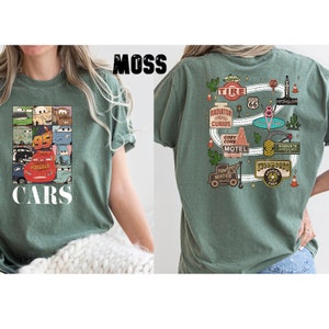 Puede incluir: Una camiseta verde con un estampado de Cars en la parte delantera y un mapa tem&aacute;tico de Cars en la parte posterior. El mapa incluye el texto "Radiator Springs Curios", "Cozy Cone Motel", "Tow Mater" y "Ribbhooks Organic Farms".