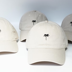 May include: Three beige baseball caps with a black palm tree embroidered on the front of each cap.