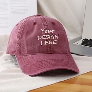 Könnte beinhalten: Eine rote, abgenutzte Baseballkappe mit einem weißen gestickten Design, das "Your Design Here" lautet.
