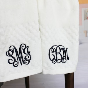 May include: Two white towels with black embroidered monograms. The monogram on the left towel is "SM" and the monogram on the right towel is "GBM".