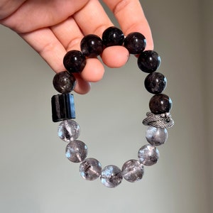 May include: A black and clear crystal beaded bracelet with a silver charm. The bracelet is made with round beads and a rectangular black bead.