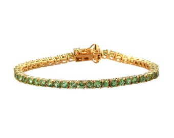Puede incluir: Un brazalete de tenis de oro con piedras preciosas verdes.