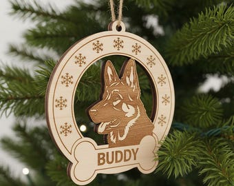 Può includere: Ornamento natalizio in legno con un disegno di pastore tedesco. L'ornamento ha una cornice circolare con ritagli di fiocchi di neve e un'etichetta a forma di osso con la scritta "BUDDY". È appeso a uno spago di spago naturale.