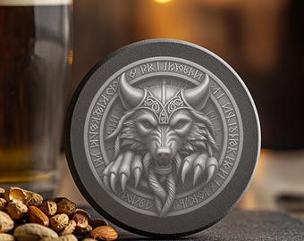 May include: A black circular coaster with a silver wolf head design. The wolf is wearing a helmet with horns and has runes around the outside of the design.