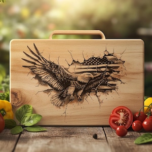 May include: A wooden cutting board with a handle, featuring an engraved design of an American bald eagle breaking through a cracked surface to reveal the American flag. The board is light brown and sits on a wooden table with fresh vegetables.