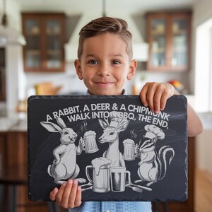 May include: A black slate sign with a white design of a rabbit, deer, and chipmunk holding mugs of beer. The sign reads "A rabbit, a deer & a chipmunk walk into BBQ, the end."