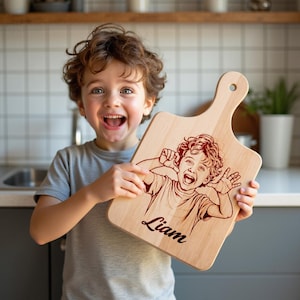 Może przedstawiać: Jasna drewniana deska do krojenia z uchwytem, z wygrawerowanym wizerunkiem dziecka robiącego śmieszną minę i imieniem "Liam" w ozdobnej czcionce. Deska trzymana jest przez uśmiechnięte dziecko.