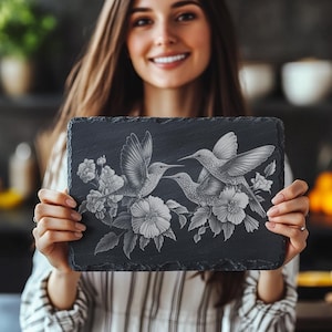 Puede incluir: Una bandeja de servir de pizarra negra con un diseño grabado de tres colibríes en vuelo, rodeados de flores.