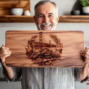 Op de afbeelding: Een rechthoekige houten snijplank met een lasergeëtst ontwerp van de Golden Gate Bridge, voedsel en bloemmotieven. Het hout heeft een natuurlijke nerf en een warme, bruine tint. De plank is ongeveer 30 cm lang.