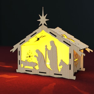 May include: A wooden nativity scene with a star on top and a light inside. The scene depicts Mary, Joseph, and baby Jesus in a manger.