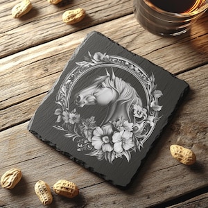 Könnte beinhalten: Ein schwarzer Schieferuntersetzer mit einer weißen Pferdekopf-Illustration, umgeben von floralen Designs. Das Pferd befindet sich in einem runden Rahmen mit verzierten Details.