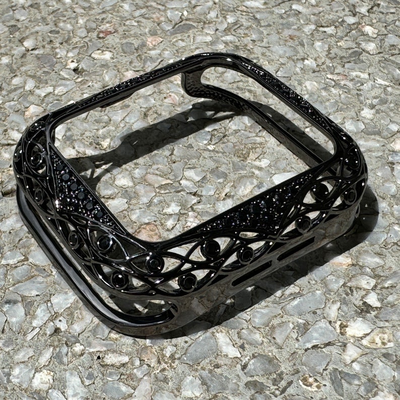 May include: Black metal Apple Watch case with a decorative, intricate design. The case has a black diamond-like finish.