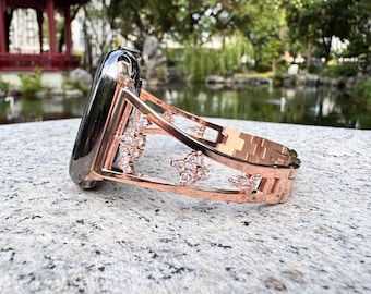 May include: A rose gold watch band with a decorative design featuring clear rhinestones. The band is made of metal and has a clasp closure.