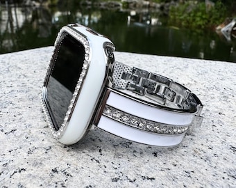 Peut inclure: Boîtier de montre Apple blanc avec un bracelet blanc et argenté orné de strass. Le boîtier a un écran transparent et une lunette blanche.