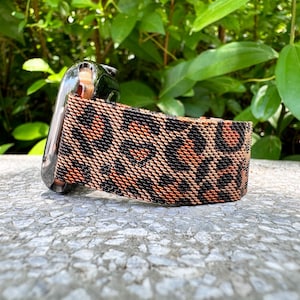 Puede incluir: Una banda de reloj de nylon tejido con estampado de leopardo negro y naranja.