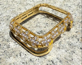 Könnte beinhalten: Ein goldfarbenes Uhrengehäuse mit floralem Design, besetzt mit klaren Kristallen. Das Gehäuse ist rechteckig mit abgerundeten Ecken und einem Bandanschluss. Die Kristalle sind in einem sich wiederholenden Muster angeordnet.