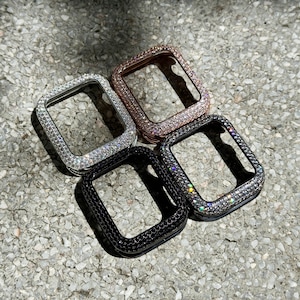 May include: Four rectangular smartwatch protective cases featuring a pavé-set crystal finish. The collection includes one silver-toned case, one rose gold-toned case, one black case, and one black case with clear crystals, all with open centers.