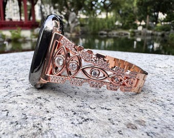 May include: A rose gold watch band with a decorative design featuring clear rhinestones. The band is made of metal and has a delicate, intricate pattern.