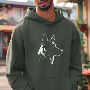 May include: Dark green hoodie featuring a white graphic of a dog's profile. The hoodie has a drawstring hood and a front pocket. The dog graphic is a minimalist design, showcasing the dog's head and neck in a side view. The hoodie is made of a soft material.