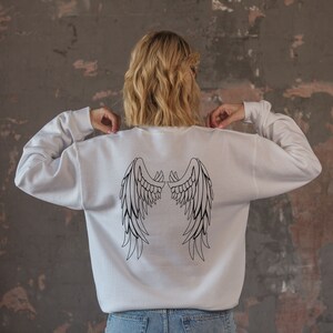 May include: White sweatshirt with a black outline of angel wings on the back.