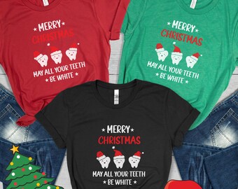 May include: Three black, green, and red t-shirts with a Christmas themed design. The design features three cartoon teeth wearing Santa hats and the text "Merry Christmas, May all your teeth be white."