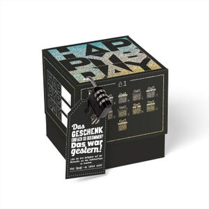 May include: A black gift box with a glittery holographic design that says "Happy Birthday". The box has a combination lock on it and a tag that says "Das Geschenk einfach so bekommen? Das war gestern!"  L&ouml;se die drei Aufgaben auf der R&uuml;ckseite, um das Zahlenschloss zu knacken. Viel Spa&szlig; - es lohnt sich!