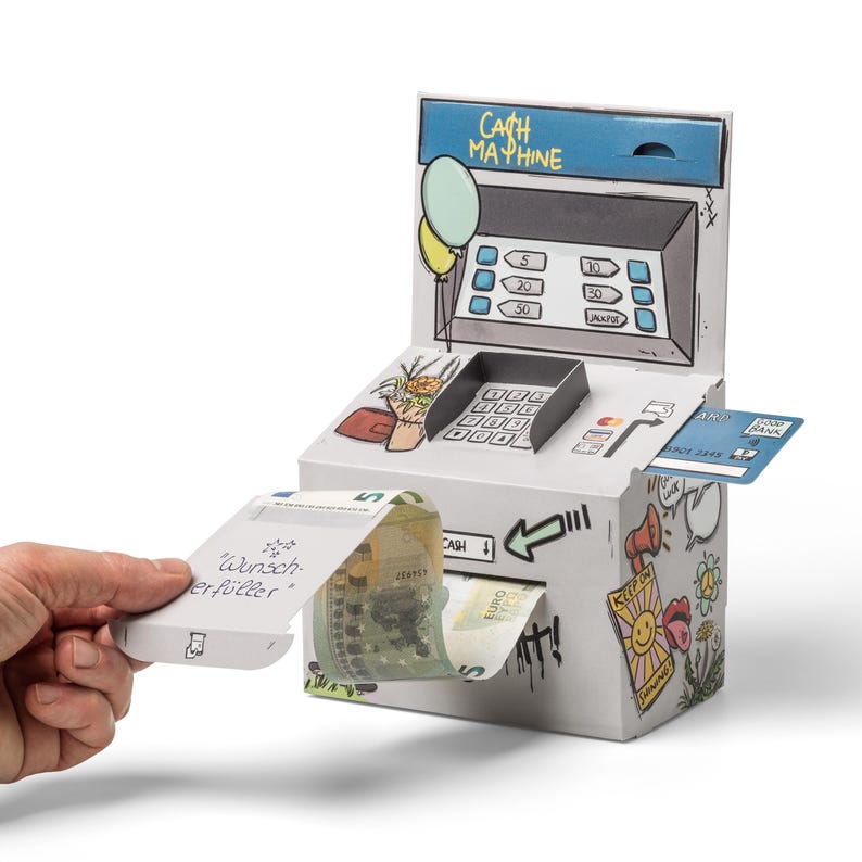 May include: A white cardboard cash machine with a cartoon design. The machine has a slot for bills and a slot for a credit card. A bill is coming out of the machine with a note that says "Wunsch erf&uuml;ller".