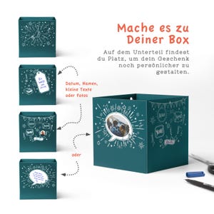 May include: A teal blue box with a white design of stars, fireworks, and speech bubbles. The box has a cut-out window to display a photo. The text "Mache es zu Deiner Box" is written in orange at the top of the image. The text "Datum, Namen, kleine Texte oder Fotos" is written in black below the box.