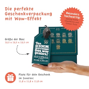 May include: A teal blue gift box with a gold glitter design and a small tag that says "Das Geschenk einfach so bekommen? Das war gestern!" The box is 12.5 cm by 12.5 cm by 12.5 cm. The box is sitting on a hand.