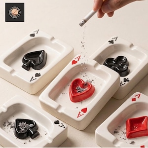 May include: A set of four rectangular ceramic ashtrays designed to resemble playing cards. Each white ashtray features a corner suit symbol and a raised, three-dimensional suit icon in the center, colored in either black or red.