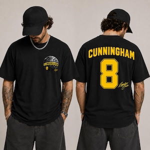 Op de afbeelding: Een zwart t-shirt met een kleine basketbalafbeelding en de tekst CUNNINGHAM 8 op de linkerborst. De achterkant toont de naam CUNNINGHAM in grote gele letters boven het nummer 8 en een gele cursieve handtekeningafbeelding.