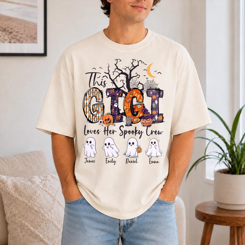 May include: An off-white short-sleeve t-shirt featuring a graphic with the text "This GIGI Loves Her Spooky Crew". The design includes large patterned letters, a crescent moon, spiderwebs, and four cartoon ghosts labeled James, Emily, Daniel, and Emma.