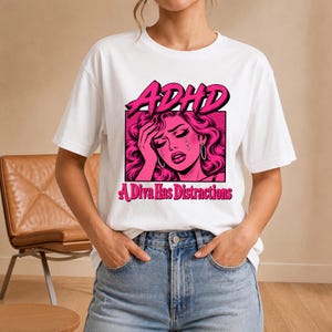 Könnte beinhalten: Ein weißes Kurzarm-T-Shirt mit einer pinkfarbenen Pop-Art-Grafik einer weinenden Person, die ihre Hand an die Stirn hält. Der Text ADHD steht über der Grafik und der Text A Diva Has Distractions ist darunter in Pink aufgedruckt.