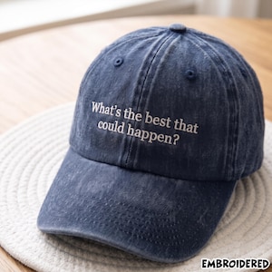Op de afbeelding: Een marineblauwe baseballpet met een verwassen, verweerde afwerking. Het voorpaneel is voorzien van wit geborduurde tekst die luidt, What's the best that could happen? De pet heeft een gebogen klep, een knoop aan de bovenkant en ventilatiegaatjes.