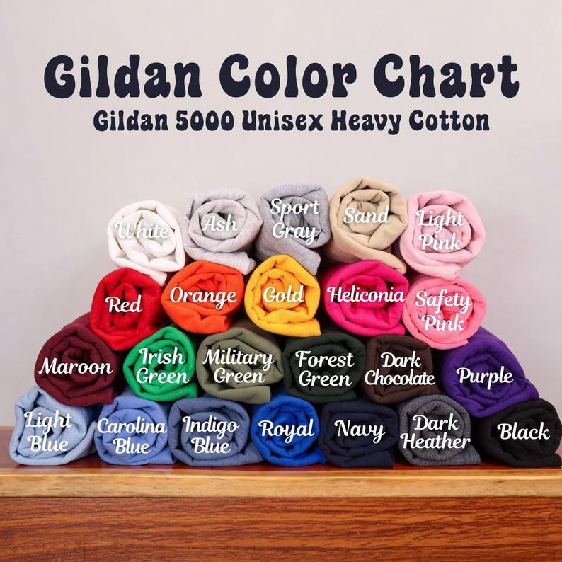 May include: A Gildan Color Chart for Gildan 5000 Unisex Heavy Cotton t-shirts, displaying a stacked arrangement of rolled fabric swatches in various colors, each labeled with its specific color name including White, Ash, Sport Gray, Sand, and Light Pink.