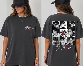 Puede incluir: Una camiseta gris carbón de manga corta con un pequeño logotipo blanco de Stray Kids en el pecho izquierdo. La parte posterior muestra una cuadrícula de ocho retratos en blanco y negro de los miembros de la banda y el logotipo de Stray Kids.